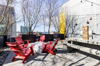 1-BR Apartments In Downtown Seattle, WA - Rooftop Lounge With Red Seating, Cement Tables, Giant Jenga, And Café Lighting.